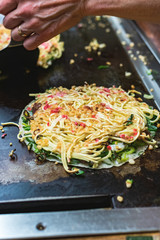 Okonomiyaki, Japanese pancake in the making. Tasty traditional dish from Hiroshima prefecture, Japan.