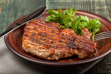 a piece of fried pork with herbs on a white dish on a wooden table, closeup view