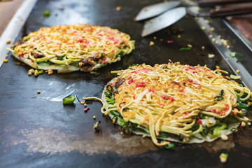 Okonomiyaki, Japanese pancake in the making. Tasty traditional dish from Hiroshima prefecture, Japan.