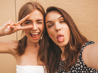 Two young smiling hipster women in summer clothes. Girls taking selfie self portrait photos on...