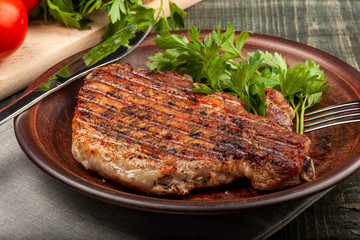 a piece of fried pork with herbs on a white dish on a wooden table, closeup view