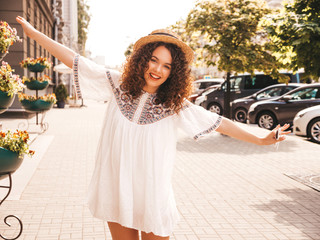 Portrait of beautiful smiling model with afro curls hairstyle dressed in summer hipster white dress. Sexy carefree girl posing in the street background. Trendy funny and positive woman having fun