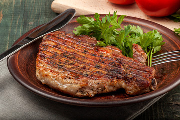 a piece of fried pork with herbs on a white dish on a wooden table, closeup view
