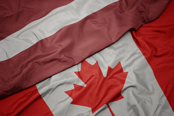 waving colorful flag of canada and national flag of latvia.