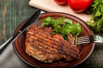 a piece of fried pork with herbs on a white dish on a wooden table, closeup view