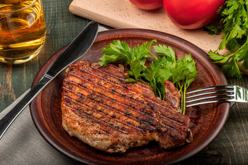a piece of fried pork with herbs on a white dish on a wooden table, closeup view
