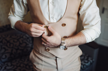 The groom in a beige suit and vest buttons a button. Waiting for the bride. Morning groom. Wedding details. Composition and concept.