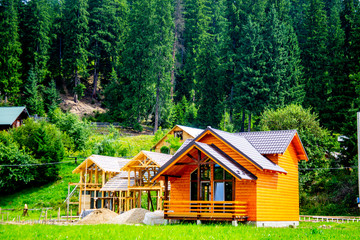 New house construction on a green lawn between two finished wooden houses. Wooden house made of logs. Building a new house from scratch in the summer. sunny day