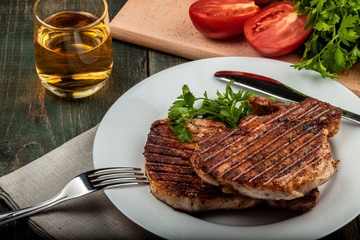 a piece of fried pork with herbs on a white dish on a wooden table, closeup view