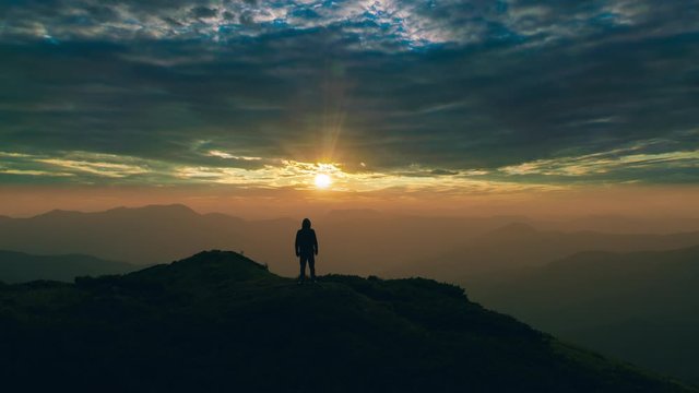 The man standing on the mountain top against a picturesque sunset