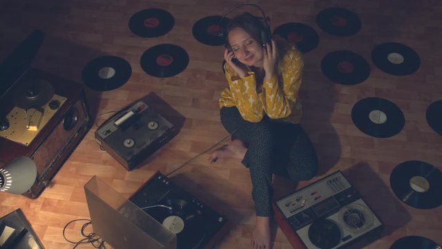 Girl listens to music surrounded by vintage devices for reproducing and recording sound.  Girl sits on floor. Next to her are bobbin tape recorders of the 60s, 70s and 80s.