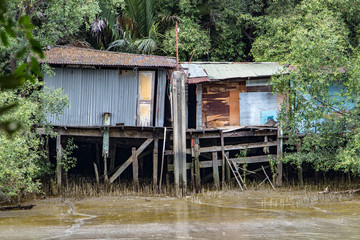 Poor houses on the muddy river bank. Metal shacks stand on wooden beams by the water.