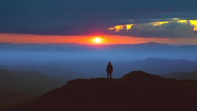 The man standing on the mountain top against a picturesque sunrise. time lapse