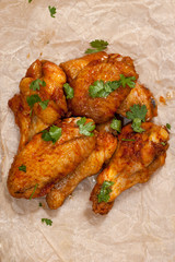 Fried juicy chicken wings marinated with honey, soy sauce, spices, sprinkled with finely chopped cilantro on a paper background. Asian recipe, top view, close-up.