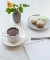 cup of hot chocolate with macarons flowers and notepad on a white background