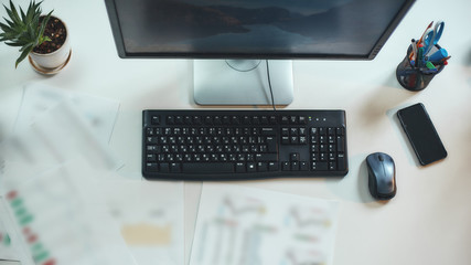 Place of work. Top view of a working place in the modern office. Computer, keyboard and mobile phone on the table