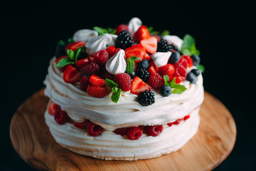 Fruit cake. Cake decorated with berries on a wooden stand on a black background.
