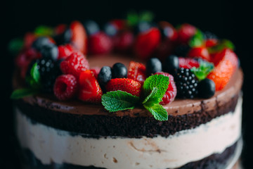 Fruit cake. Cake decorated with berries on a wooden stand on a black background.