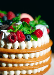 Fruit cake. Cake decorated with berries on a wooden stand on a black background.
