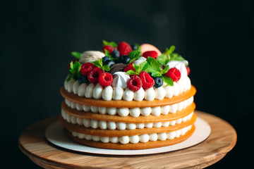 Fruit cake. Cake decorated with berries on a wooden stand on a black background.