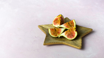 Arrangement of fresh cut figs on golden wooden plate on light pink background, copy space, banner. Selected focus