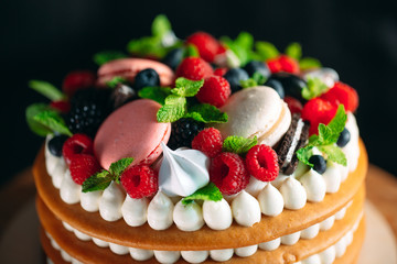 Fruit cake. Cake decorated with berries on a wooden stand on a black background.