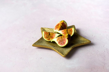 Arrangement of fresh cut figs on golden wooden plate on light pink marbled background with copy space. Selected focus