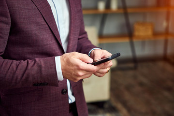 Male businessman in a stylish jacket conducts business correspondence holding smartphone