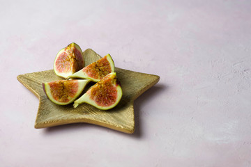 Arrangement of fresh cut figs on golden wooden plate on light pink marbled background with copy space. Selected focus
