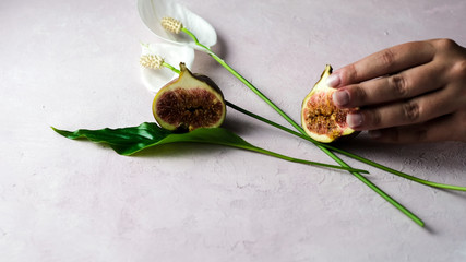 Hand holding a fresh whole and cut figs with some flowers on a light pink marbled background, copy space. Selected focus