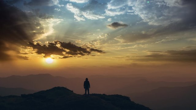 The man standing on a mountain top against a bright sunset. time lapse
