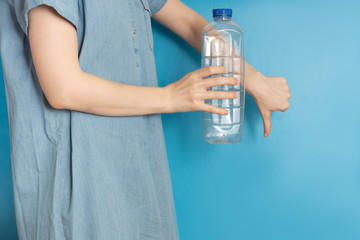 Woman holds a plastic bottle on blue background. Life concept without plastic