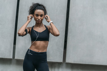 Fototapeta premium Fitness woman taking a break from outdoor training session with earphones and look in camera