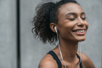 Close up shot of happy female runner smiling against grey background. African female with earphone...