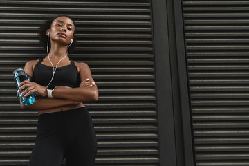 Athletic woman taking a break during workout with earphones and bottle of water in hand