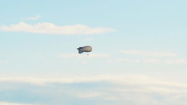 White airship flying with tourists on a background of blue sky with clouds 4K.