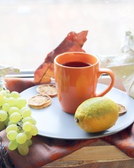  Orange cup with a drink on the background of a window, behind which rain, fruits, a warm scarf, leaves, autumn season, the concept of home comfort