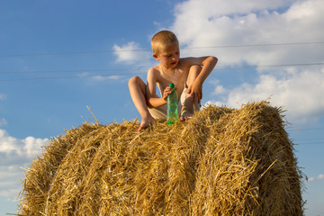 Naklejka na ściany i meble boy sitting on hay in the field,vacations on wheat field with hay bale