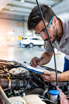 Technician with safety glasses checking the engine of a car during a vehicle inspection
