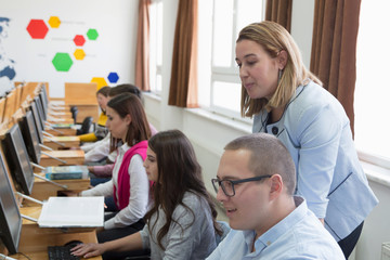 Female attractive professor explain lesson to students and interact with them in the classroom.Helping a students during class. University student being helped by female lecturer during class.