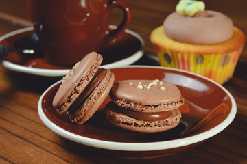 Chocolate Macaroons on a Plate with Coffee and a Cupcake on a Wood Surface