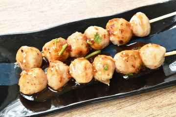 grilled pork tendon meat ball stabbing in wooden stick dressing spicy and sweet sauce on black plate 