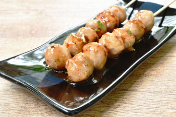 grilled pork tendon meat ball stabbing in wooden stick dressing spicy and sweet sauce on black plate 