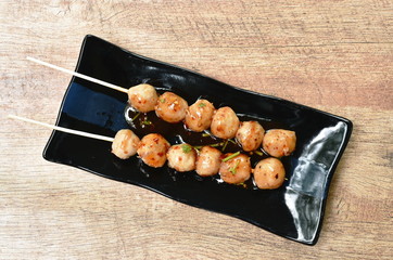 grilled pork tendon meat ball stabbing in wooden stick dressing spicy and sweet sauce on black...