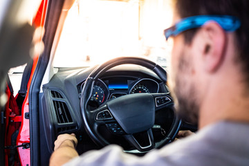 Technician with safety glasses starting the engine of a car during a vehicle inspection