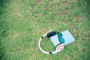 Naklejka premium White headphone, blue book and black eye glasses spectacles gadget on green grass