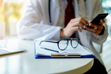 Close up glasses. Doctor using mobile phone and text messaging in the office.