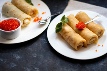 Pancakes stuffed with salted cottage cheese. In the bowl and spoon are red caviar and sour cream. Decorated with mint leaves. 