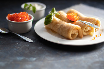 Pancakes stuffed with salted cottage cheese. In the bowl and spoon are red caviar and sour cream. Decorated with mint leaves. 