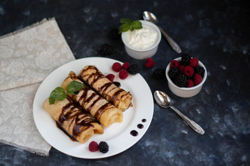 Pancakes with curd filling. Watered with chocolate topping on top, decorated with raspberries and blackberries. In bowls of berries and curd cream. 